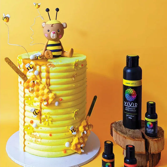 yellow cake with bees and a bear in a bee costume beside bottles of food colour