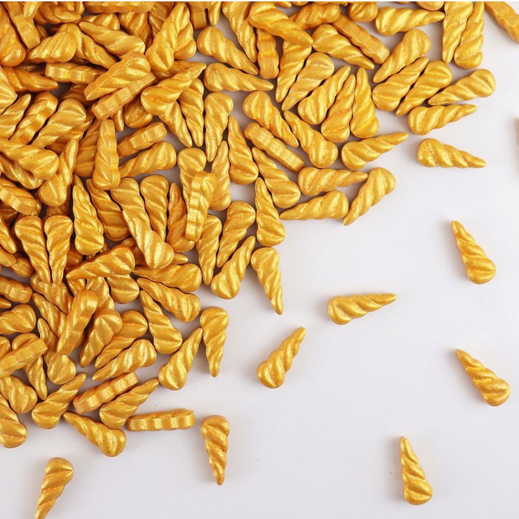 gold unicorn horn shaped sprinkles scattered on a white background