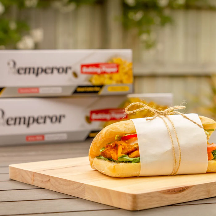 Sandwich wrapped in paper on a wooden board with 'Emperor' products in the background.