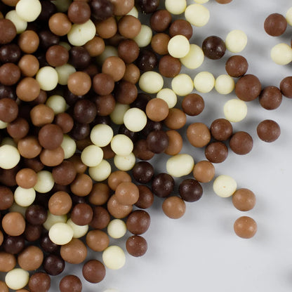 Close-up of choccy toppy choc pearls in a mix of white, dark and milk chocolate on a white surface