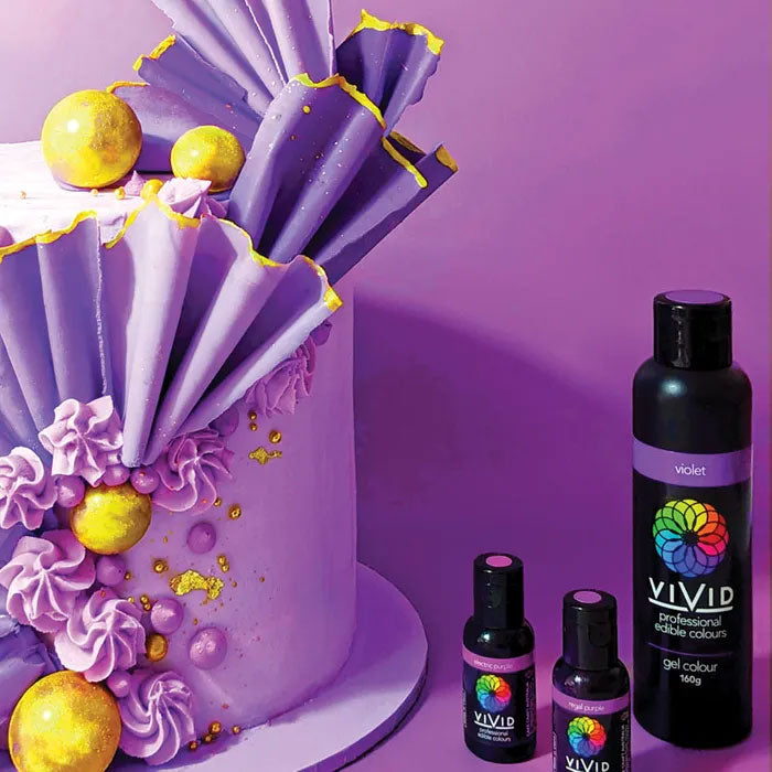 purple cake with gold decorations next to bottles of vivid gel food colouring