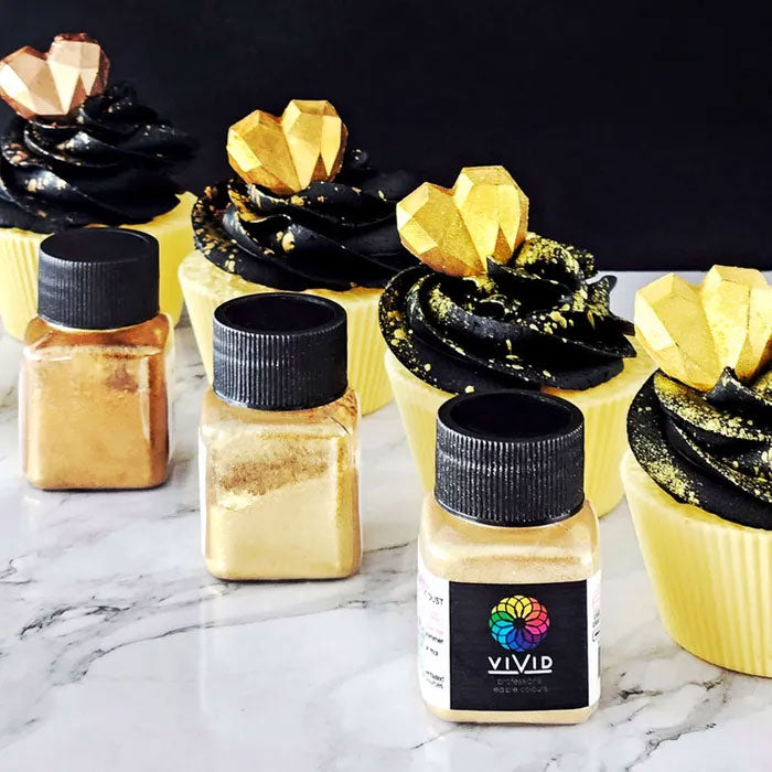 gold and black cupcakes with hearts on to beside jars of edible lustre dust