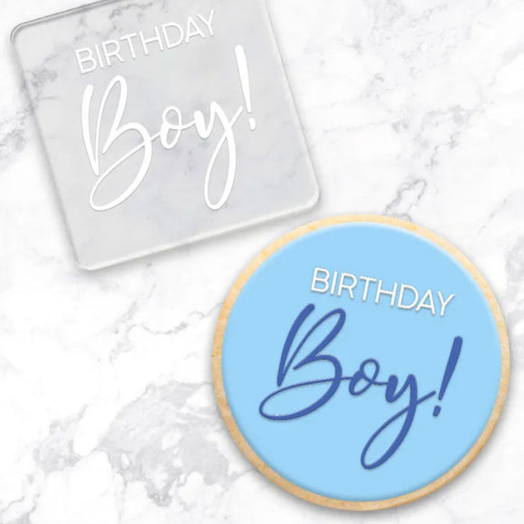 clear debosser with Birthday boy pattern beside cookie with blue icing and example with a marble background
