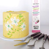 cake craft buttercream palette knives beside a yellow buttercream cake with white flowers, blue sprinkles and green leaves on a white cake board