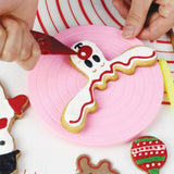 reindeer head shaped cookie being decorated with white and red icing on pink mini cookie turntable