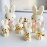 white chocolate small and medium bunnies with gold and pink ribbon around neck beside birds nest of chocolate eggs