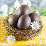 Smooth Chocolate Eggs in a birds nest with white and yellow flowers and sitting on a yellow cloth