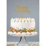 Gold glitter acrylic happy birthday cake topper atop white buttercream cake covered in rainbow confetti sprinkles atop glass cake stand