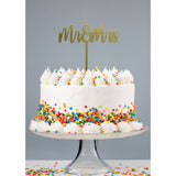 Gold mr & Mrs Acrylic Cake Topper atop white buttercream cake covered in rainbow confetti sprinkles on glass cake stand