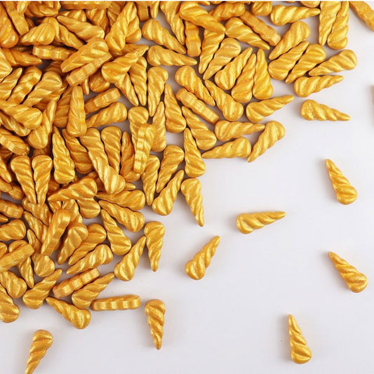 gold unicorn horn shaped sprinkles scattered on a white background