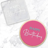 clear debosser with a Happy Birthday script pattern beside a cookie with pink icing and happy birthday in blue and white writing on a marble background