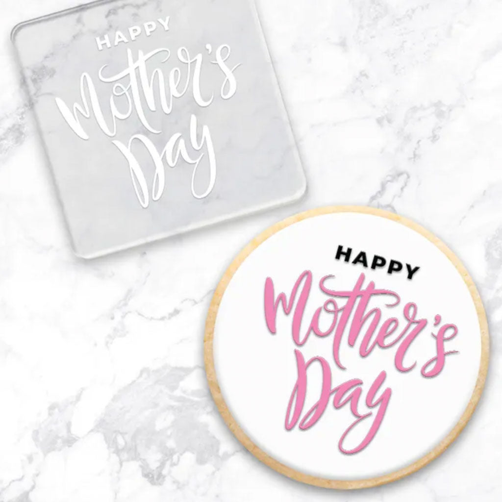 clear debosser with a Happy Mothers Day pattern beside a cookie with white icing and black and white writing on a marble background