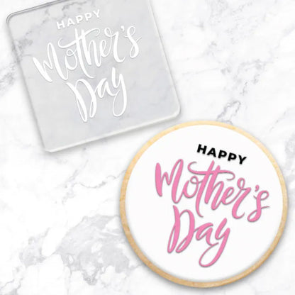 clear debosser with a Happy Mothers Day pattern beside a cookie with white icing and black and white writing on a marble background