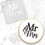clear debosser with Mr & Mrs pattern beside cookie with white icing and black writing displayed on a marble background