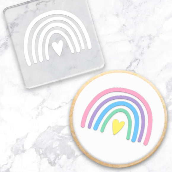 clear debosser with rainbow & heart pattern beside cookie with white icing and pink, purple, blue, green rainbow with a marble background