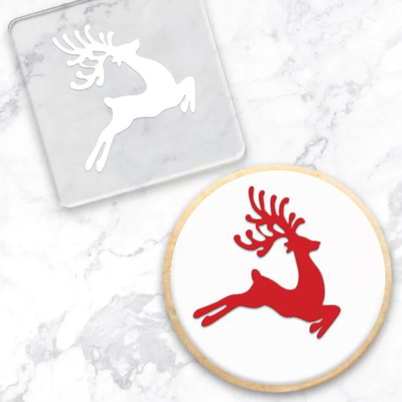 clear debosser with reindeer pattern beside cookie with white icing and red reindeer with a marble background
