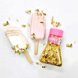 jar of loose gold leaf flakes beside one pink and one white cake pop decorated with gold leaf scattered