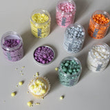 assorted colours of the bubble bubble sprinkle mix on a grey background with some sprinkles scattered