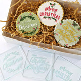 white box with cookies decorated using debossers with gold red green white writing and white green icing surrounded by brown shredded paper and debossers beside